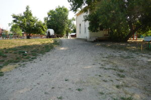 A dirt path leads between a white building and a covered wagon. 