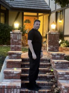 Richard, a white man, stands in front of a brick set of stairs of a house