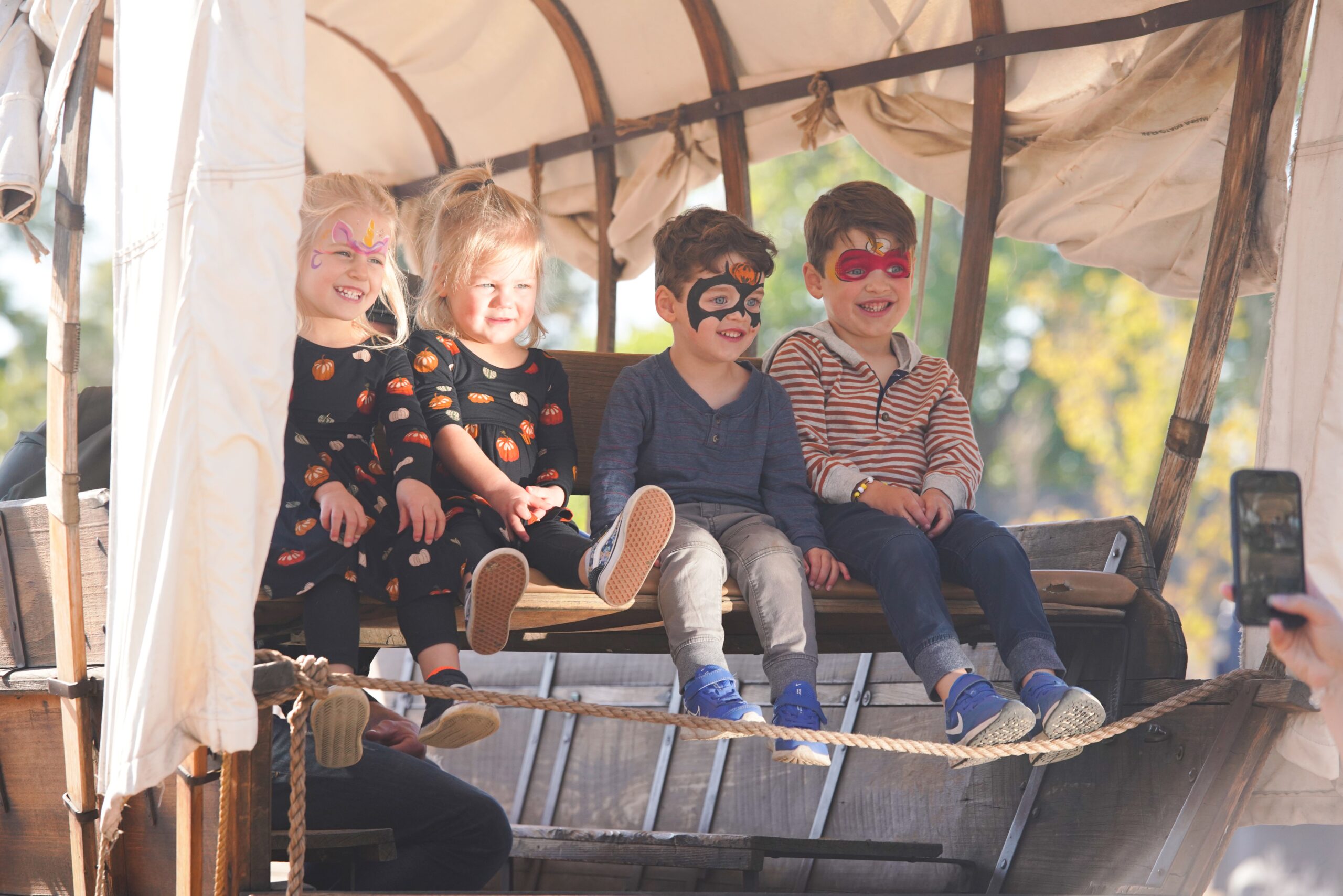Four children with face paint sit on a wagon