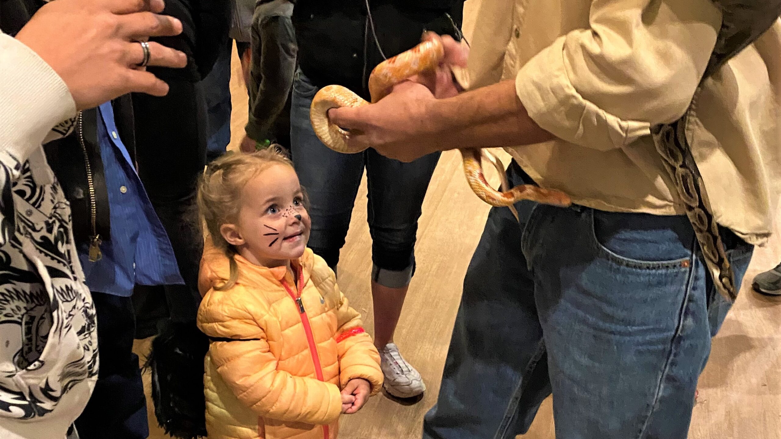 A little girl faces a man holding a snake.