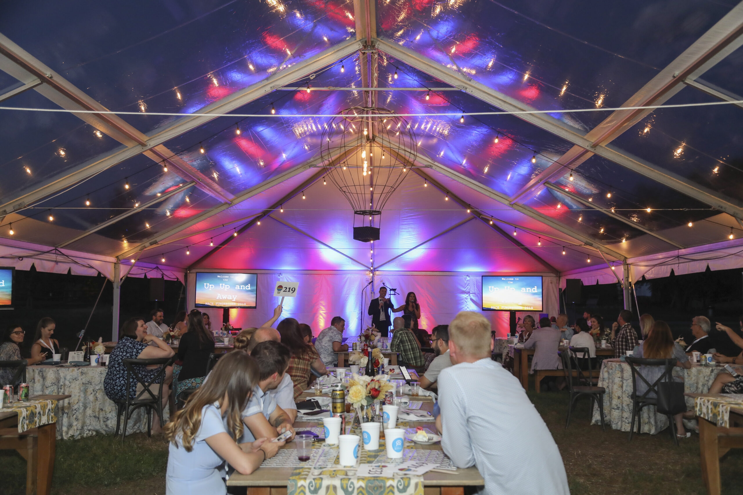 People gathered under a tent with screens showing 