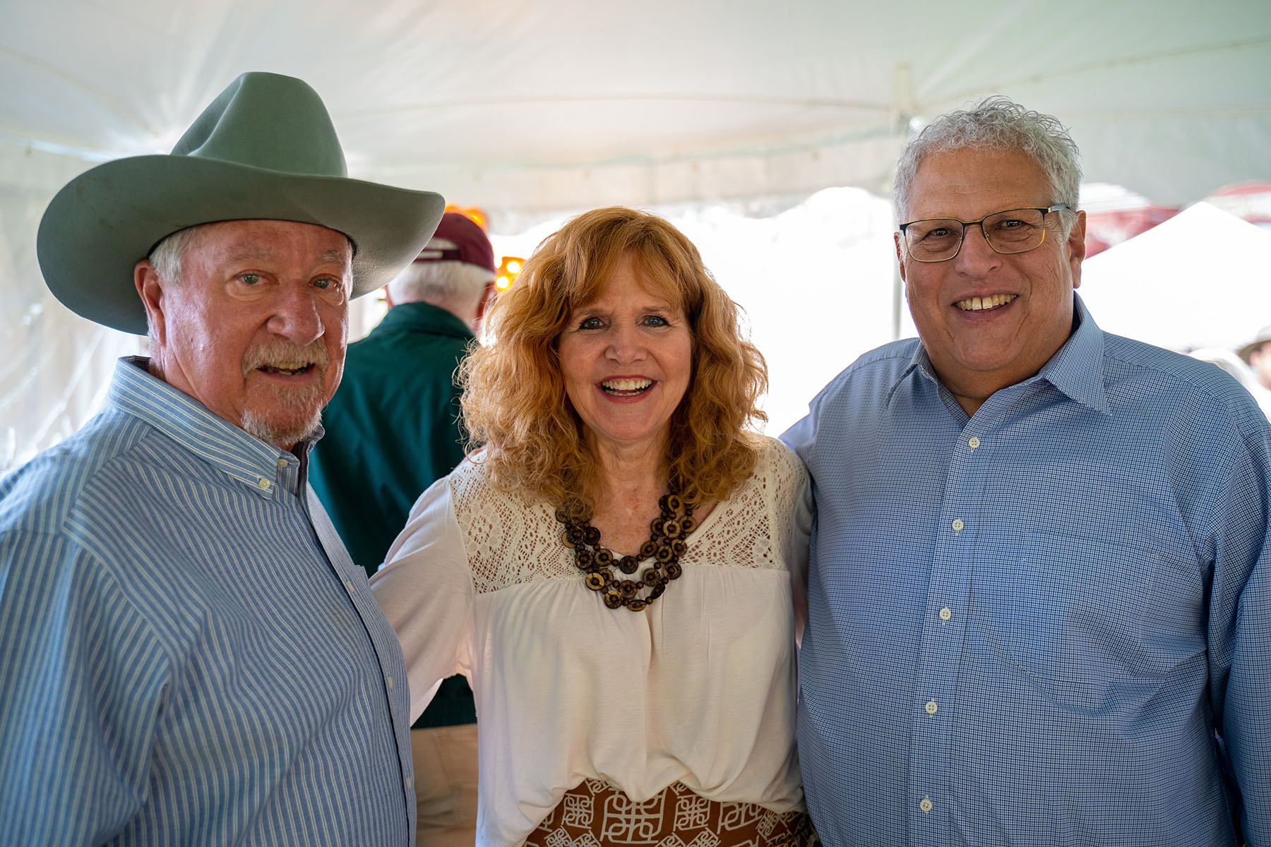 Three people smiling, including a man in a cowboy hat