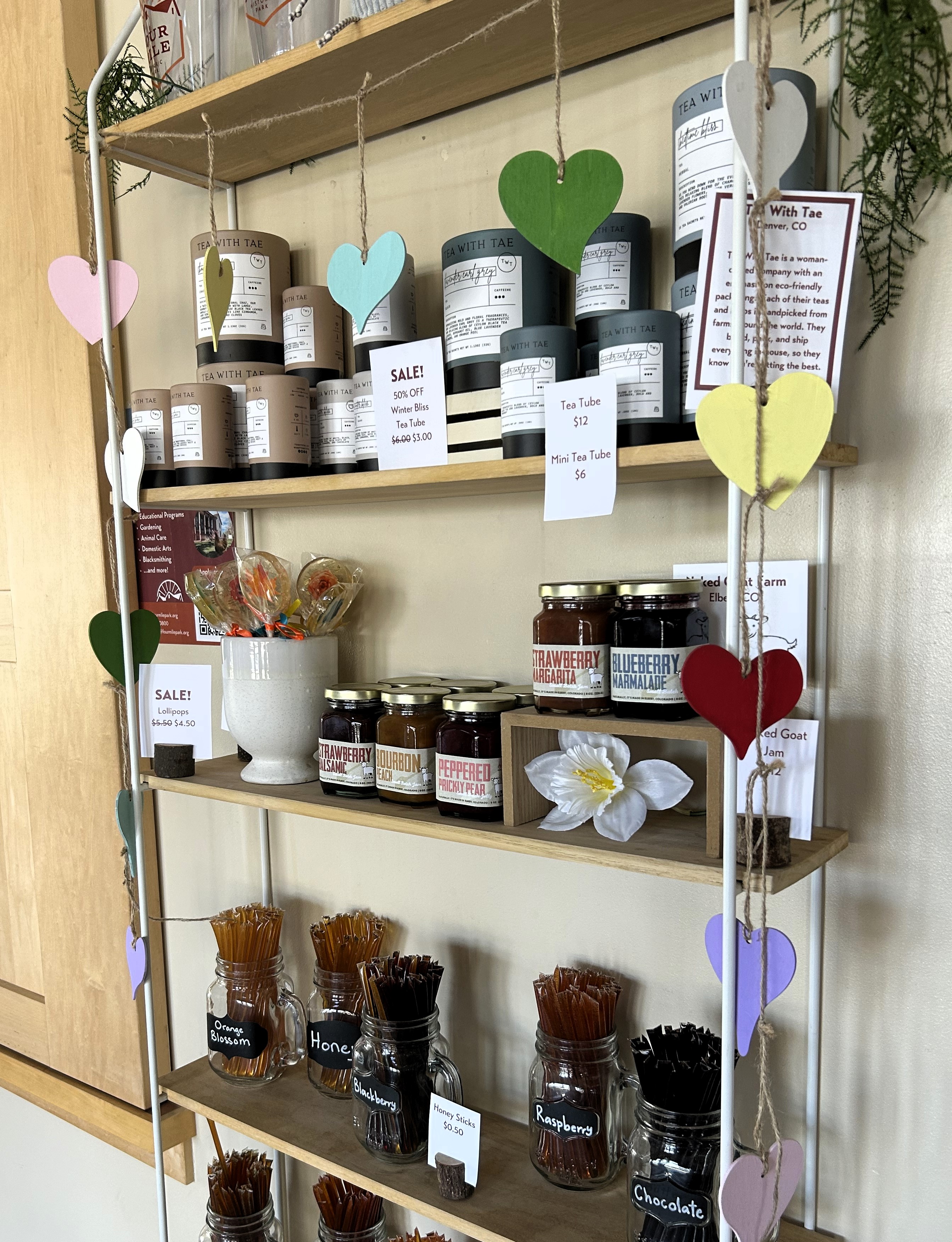 A shelf displaying various teas, jams, and honey sticks.