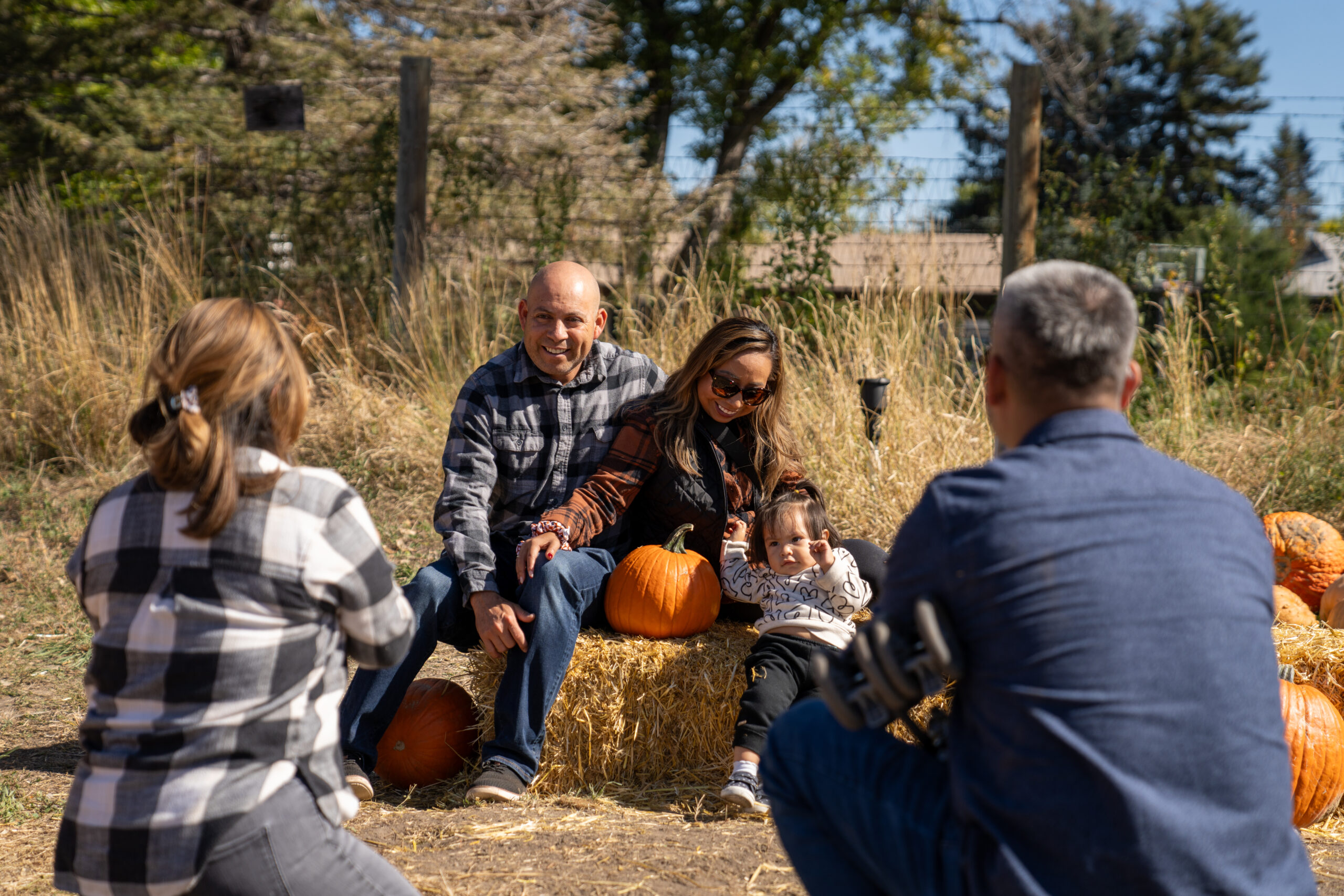 A family sitting on hay with pumpkins in fall.