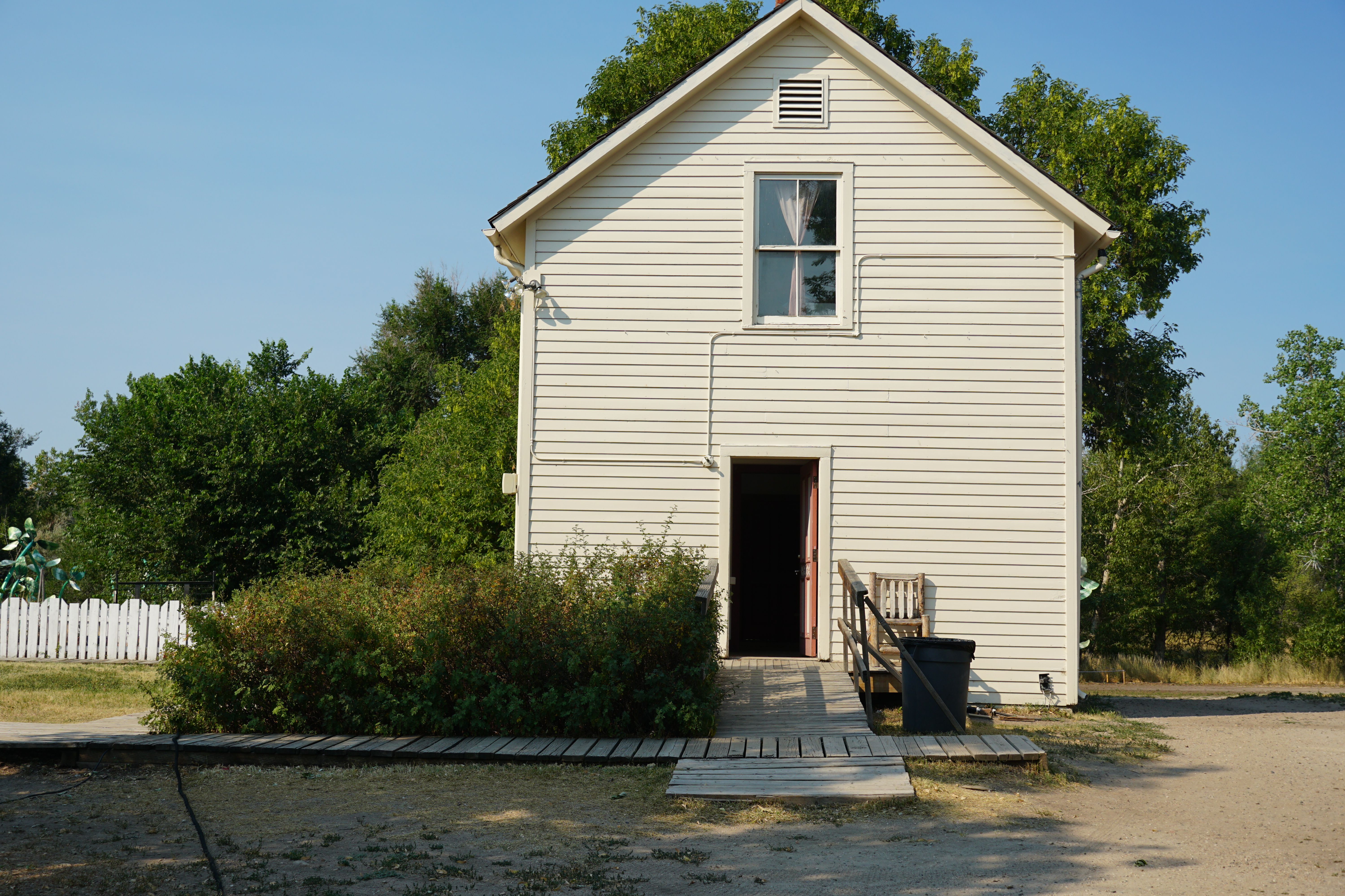 Dirt and wood path leading to a white building with the door open.