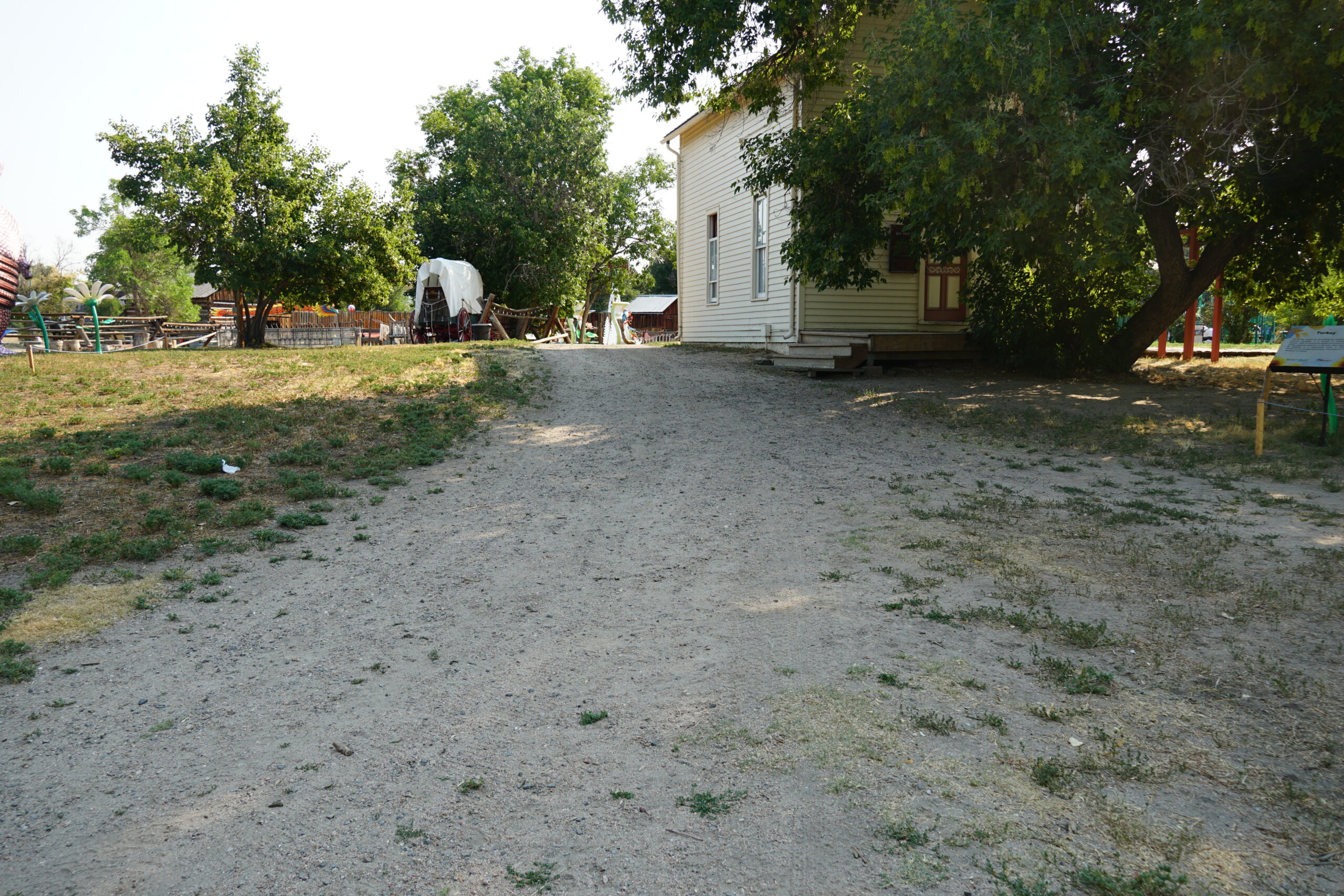 A dirt path leads between a white building and a covered wagon.