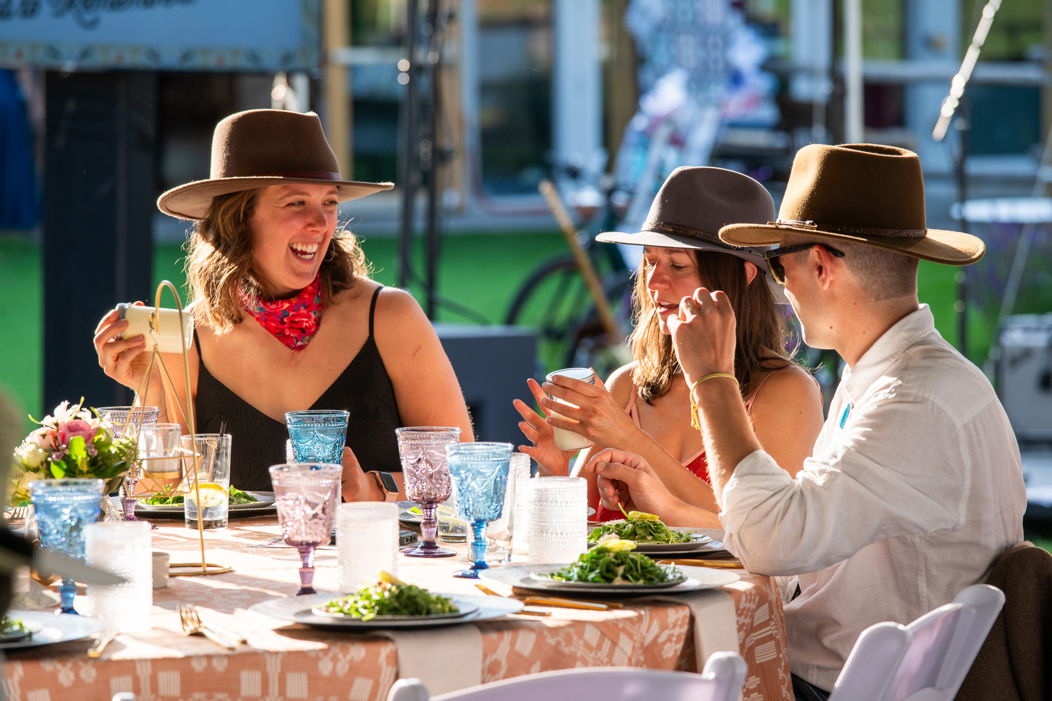 Tres personas con sombrero disfrutando de una comida al aire libre bajo el sol, riendo
