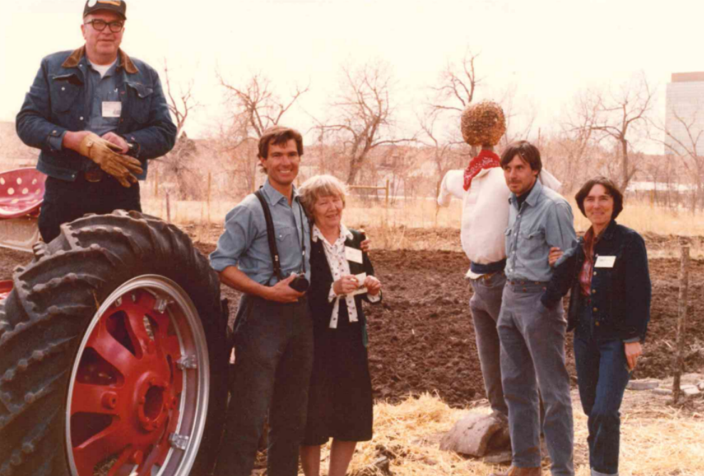 Group of people standing near a tractor and scarecrow in a rural setting
