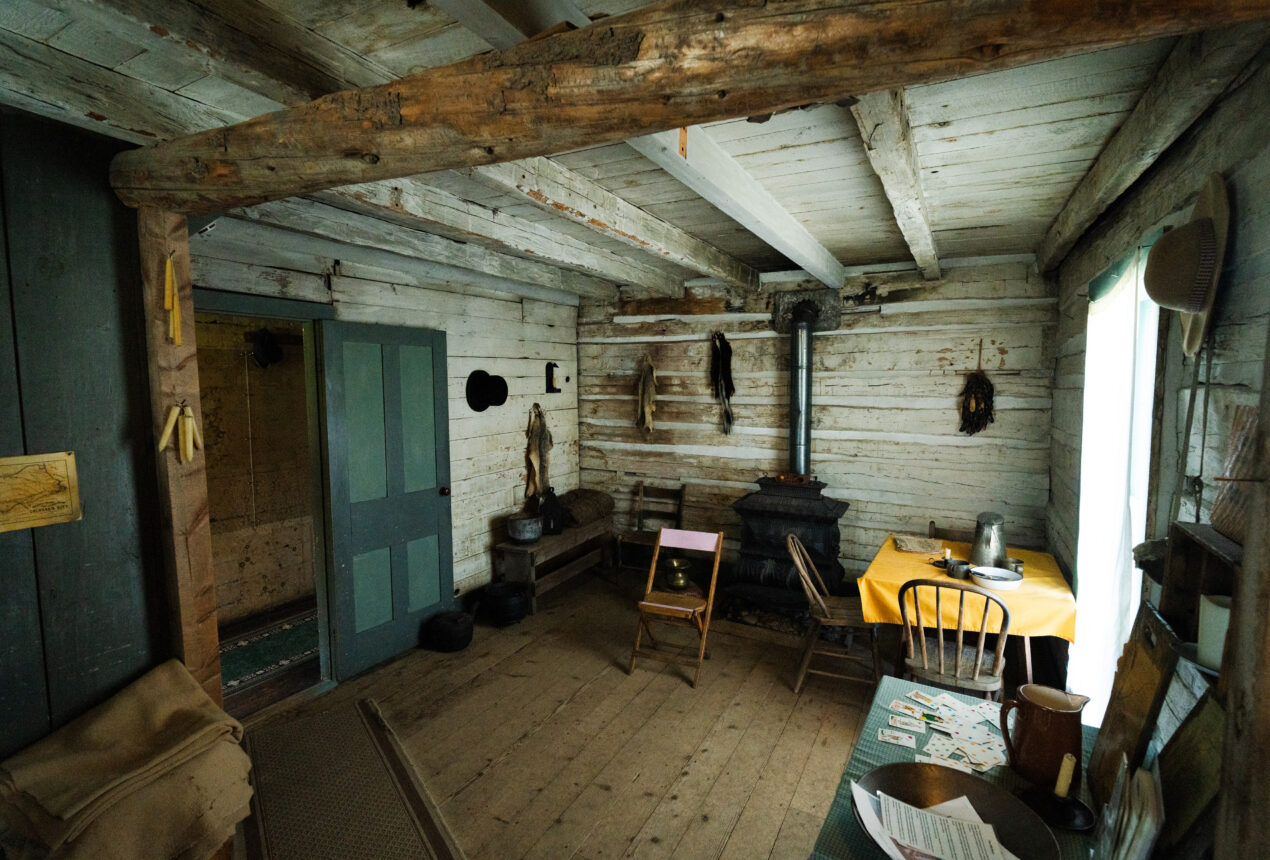 Rustic wooden cabin interior with stove, chairs, and table