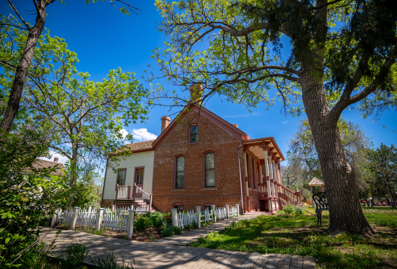 Historic park house with brick and wood siding, surrounded by lush greenery and bright blue sky