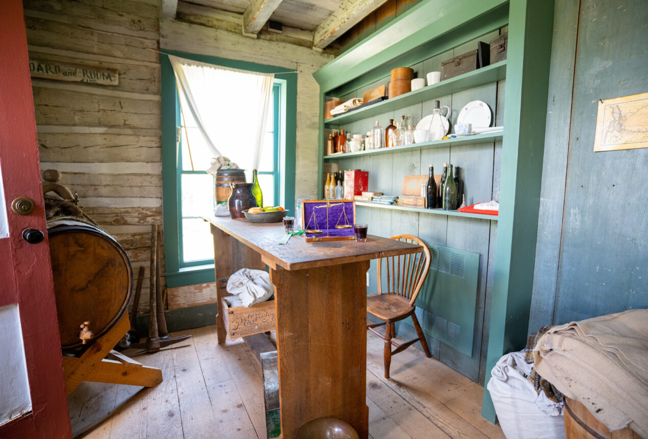 Historic rustic room with wooden furniture, shelves of bottles, and a "Board and Room" sign