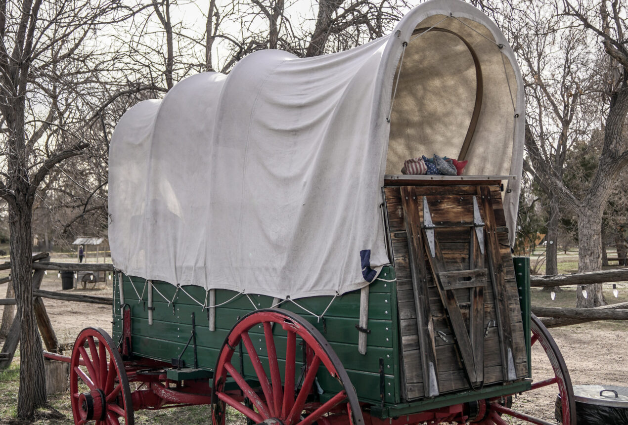 Covered wagon with red wheels in a wooded outdoor setting