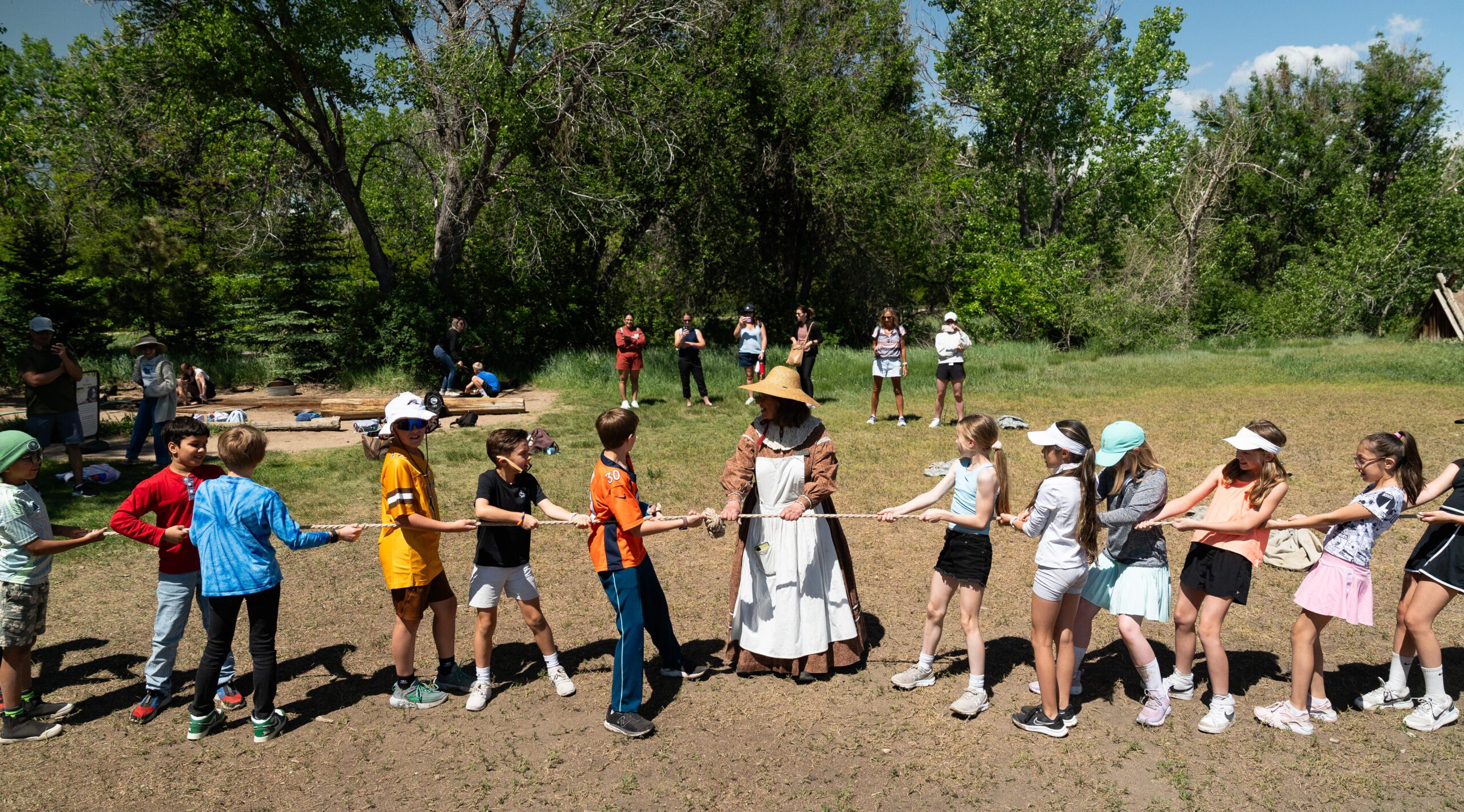 Children and an adult in costume play tug-of-war outdoors