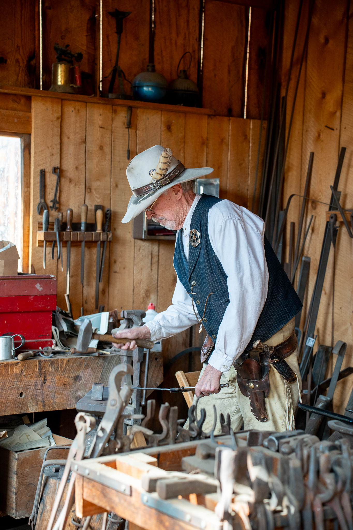 Blacksmith in cowboy hat shaping metal on a wooden bench in rustic workshop