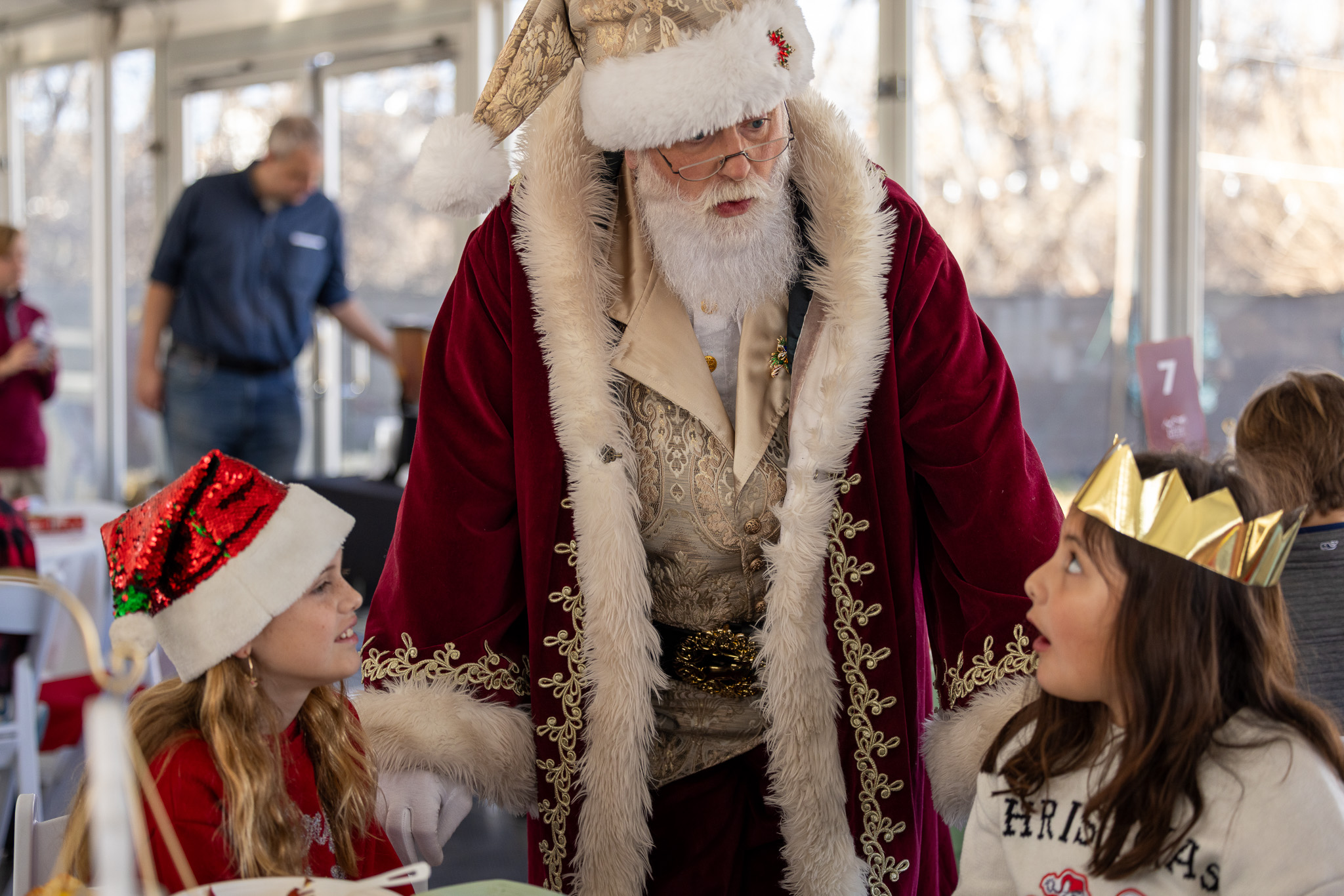 Santa interacting with two children, one wearing a red Santa hat, the other with a gold paper crown