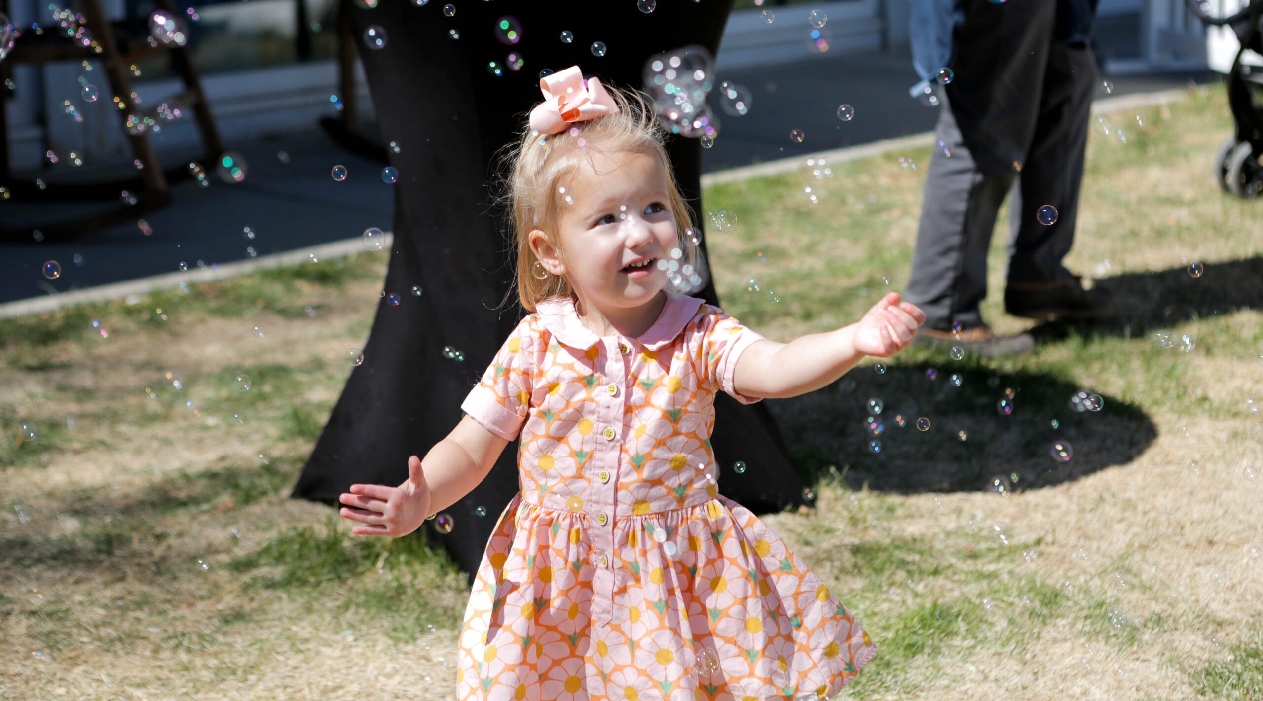 Una niña pequeña con un vestido de flores intenta atrapar con alegría las pompas de jabón en el exterior